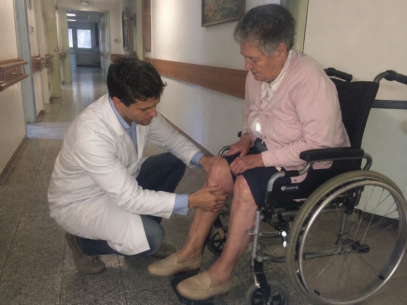 Il Dott. Marco Rossi visita il ginocchio di un paziente anziano in una casa di riposo